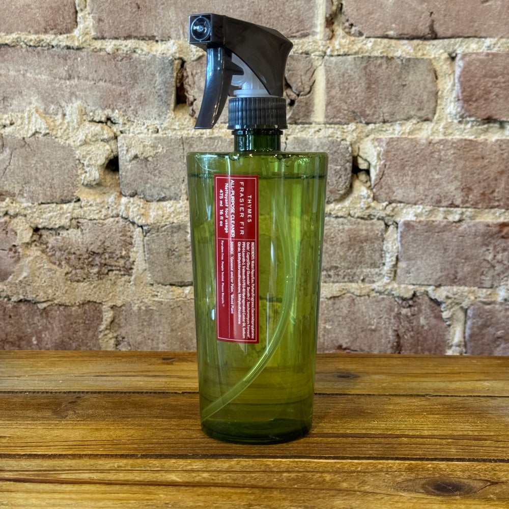 Green spray bottle with a red label on a wooden surface against a brick wall.
