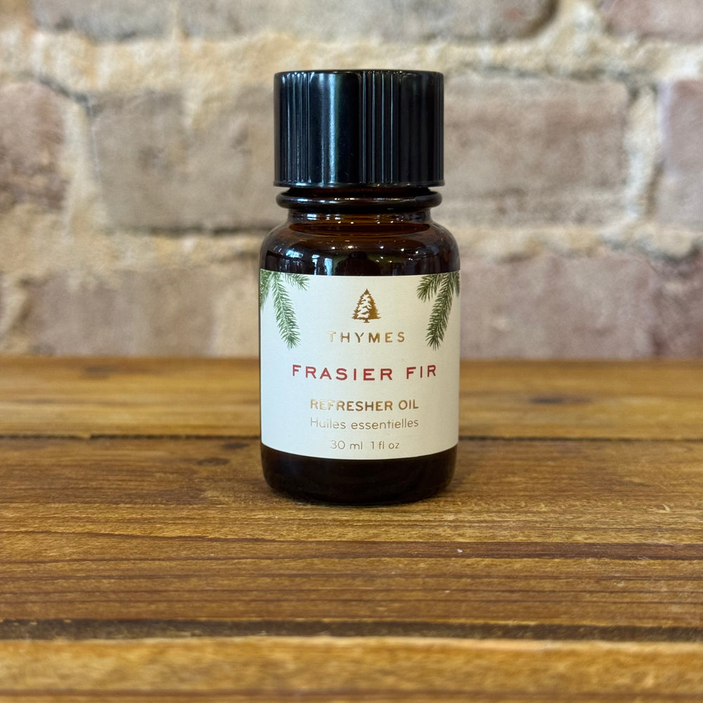 Thymes Frasier Fir refresher oil bottle on a wooden surface with a stone wall background