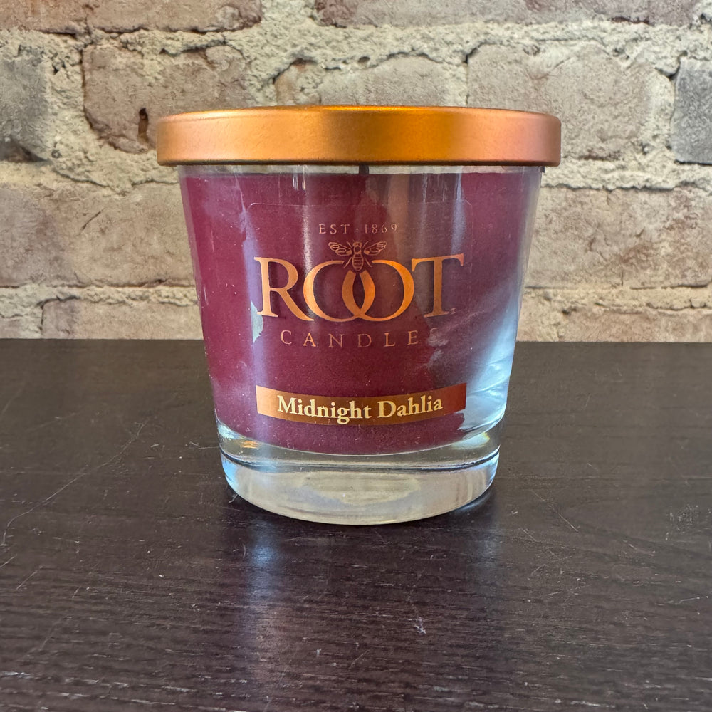 Root Candle labeled 'Midnight Dahlia' on a dark surface with a stone wall background