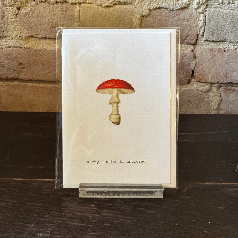 Greeting card with a red and white mushroom design on a wooden surface and stone wall background.