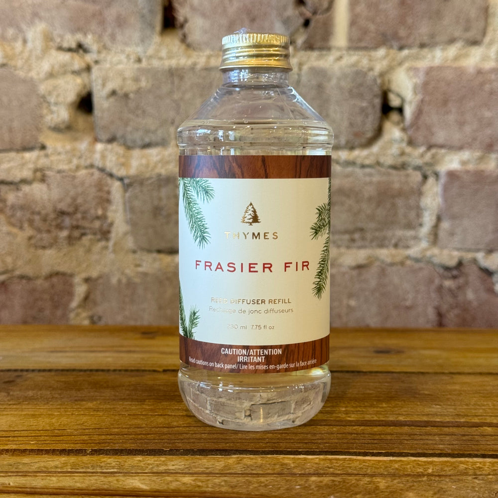 Thymes Frasier Fir diffuser refill bottle on a wooden surface with a brick wall background