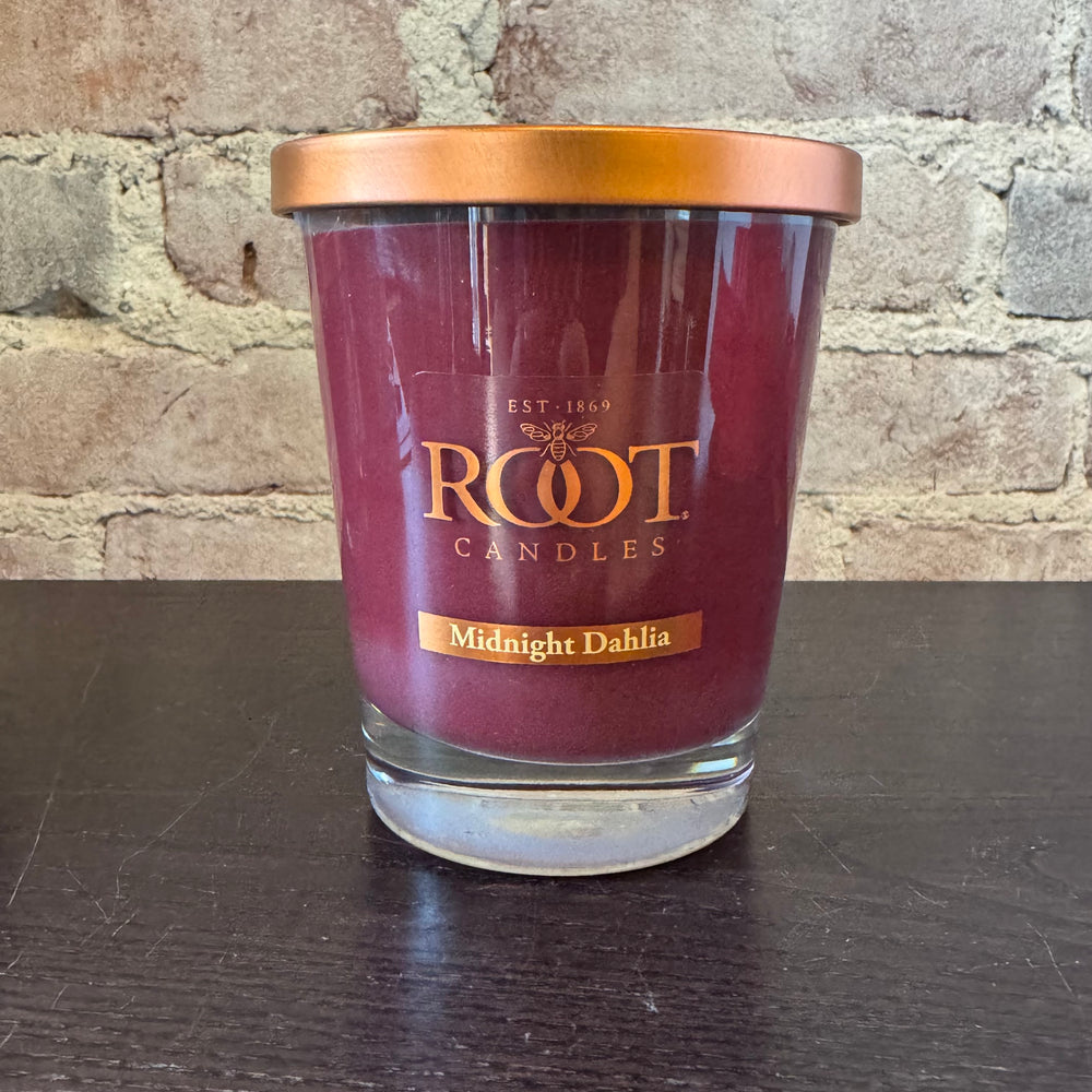 Root Candles Midnight Dahlia candle on a dark surface with a brick wall background