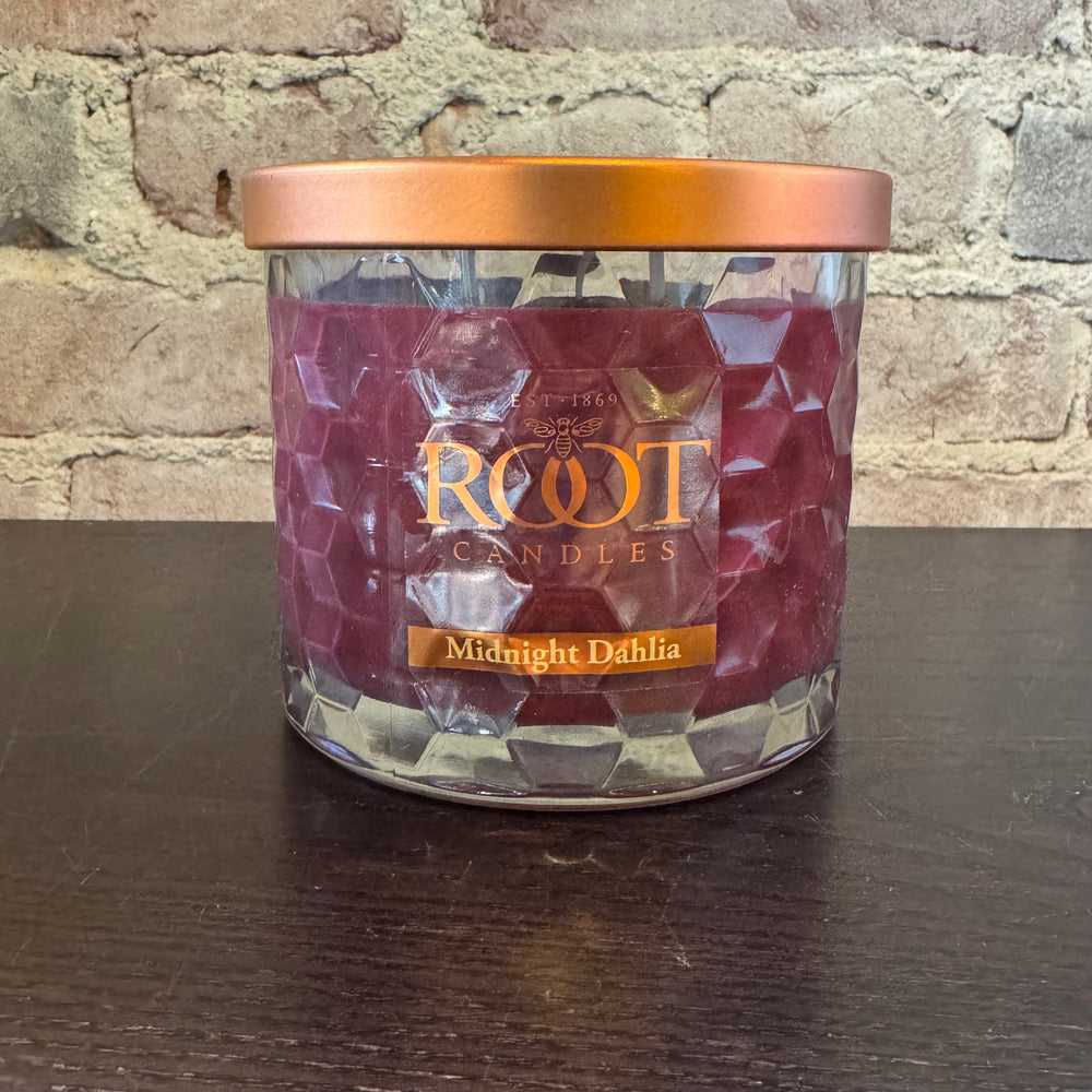 Root Candles Midnight Dahlia candle in a glass jar with a bronze lid on a wooden surface.