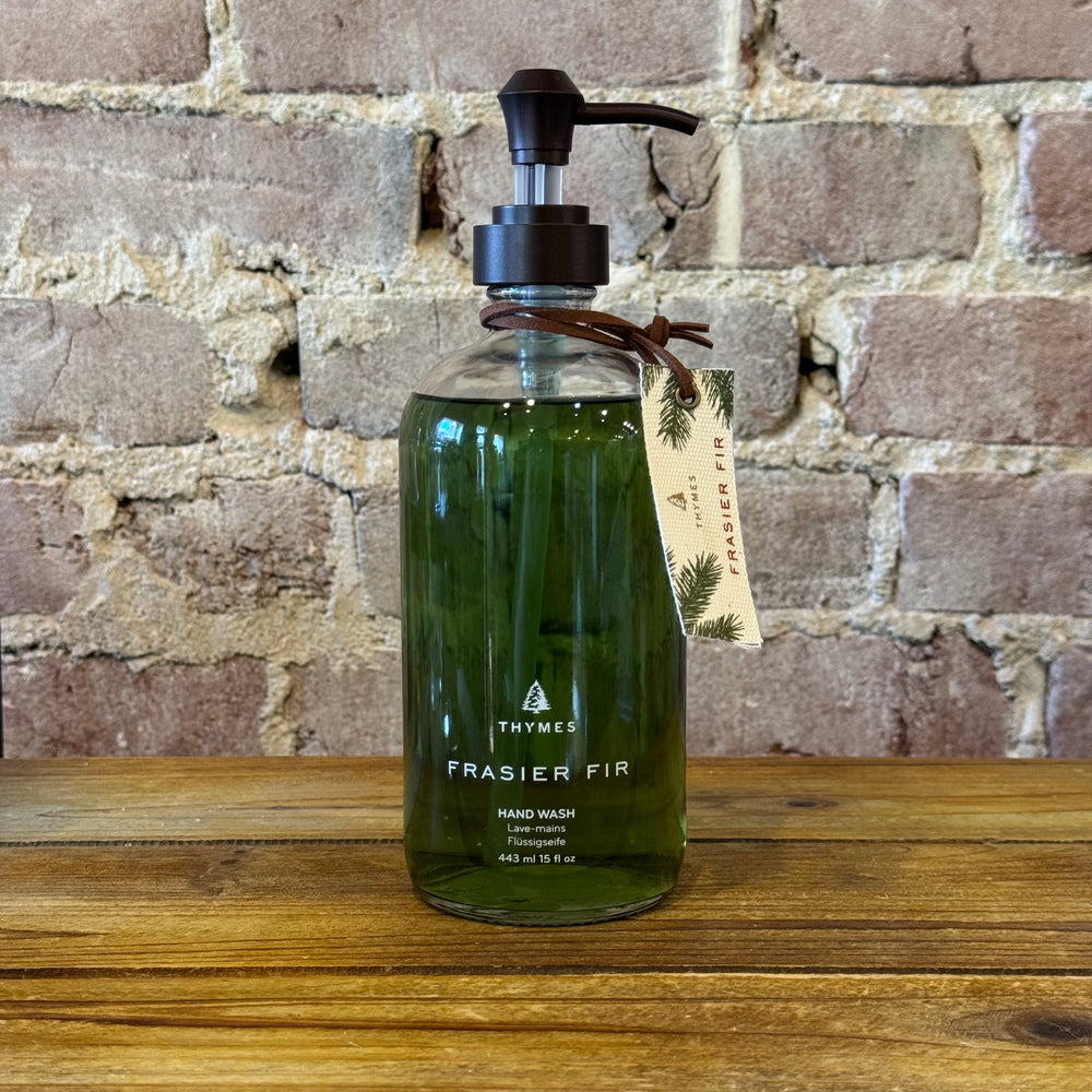 Green hand wash bottle with pump and label on a wooden surface against a brick wall.