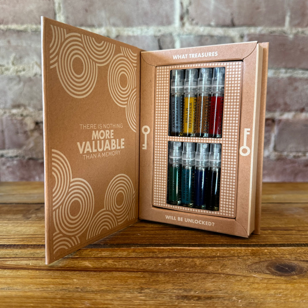 Open box with a key design and sample perfume set inside, on a wooden surface with a brick wall background.