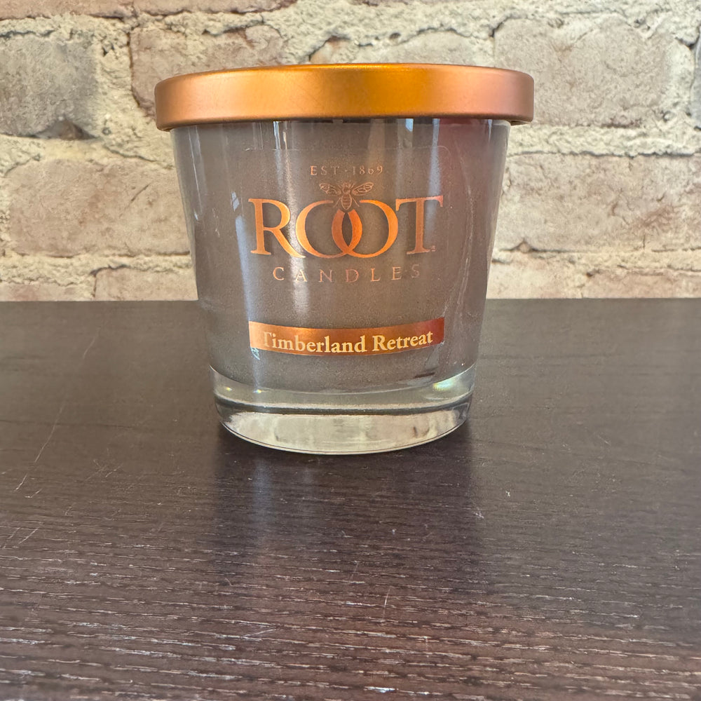 Clear Root Candles jar with copper lid on a dark surface against a brick wall background
