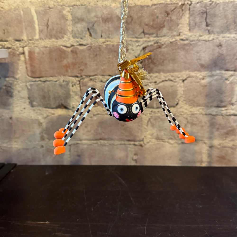 Decorative spider ornament with orange body and black and white legs hanging against a brick wall.