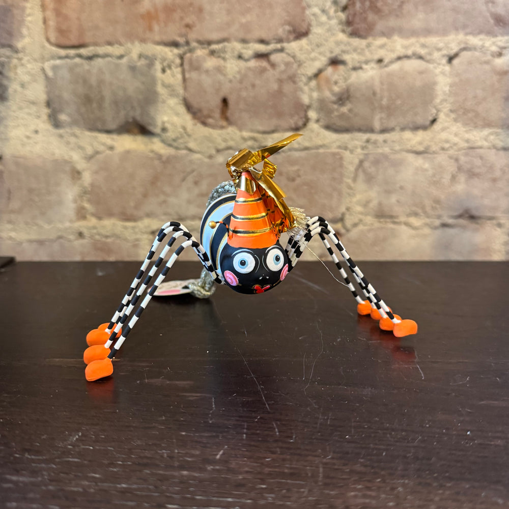 Colorful spider ornament with a Halloween hat on a wooden surface against a brick wall background