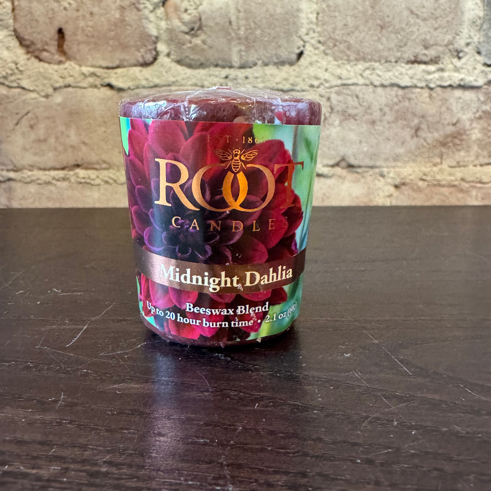 Root votive Candle Midnight Dahlia on a dark surface with a brick wall background