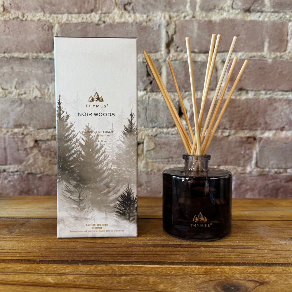 Thymes Noir Woods reed diffuser with packaging against a brick wall background