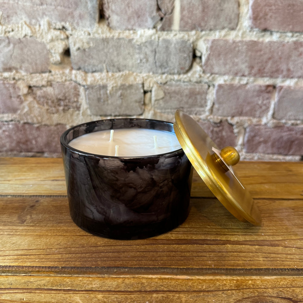 Black candle jar with a gold lid on a wooden surface against a brick wall background