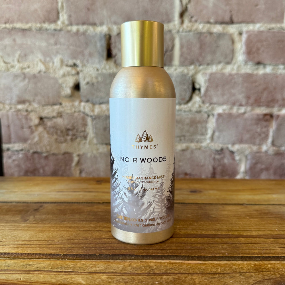 Thymes Noir Woods fragrance mist bottle on a wooden surface with a brick wall background