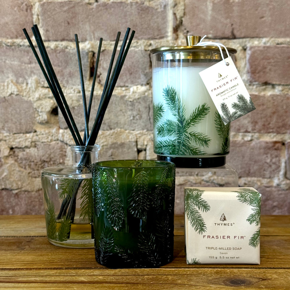 Frasier Fir candle, diffuser, and soap on a wooden surface with a brick wall background