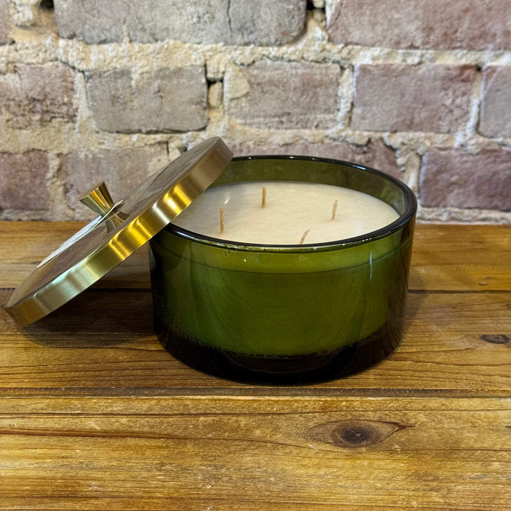 Green candle with a gold lid on a wooden surface against a brick wall background