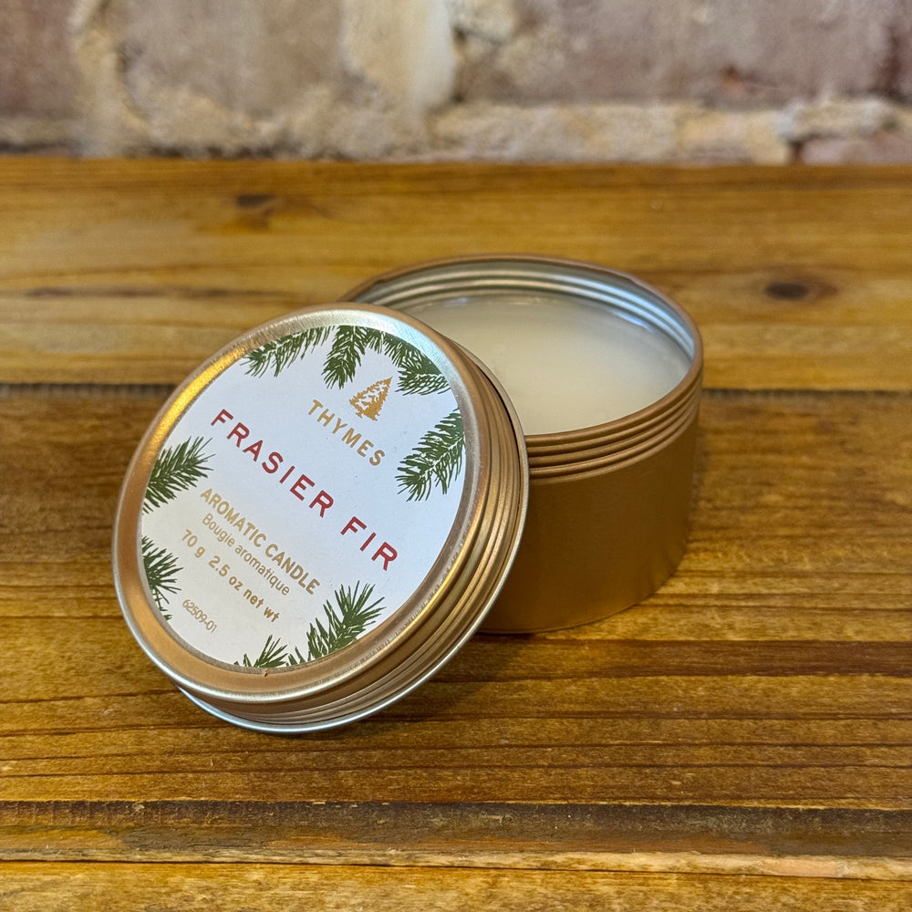 Thymes Frasier Fir tin candle on a wooden surface