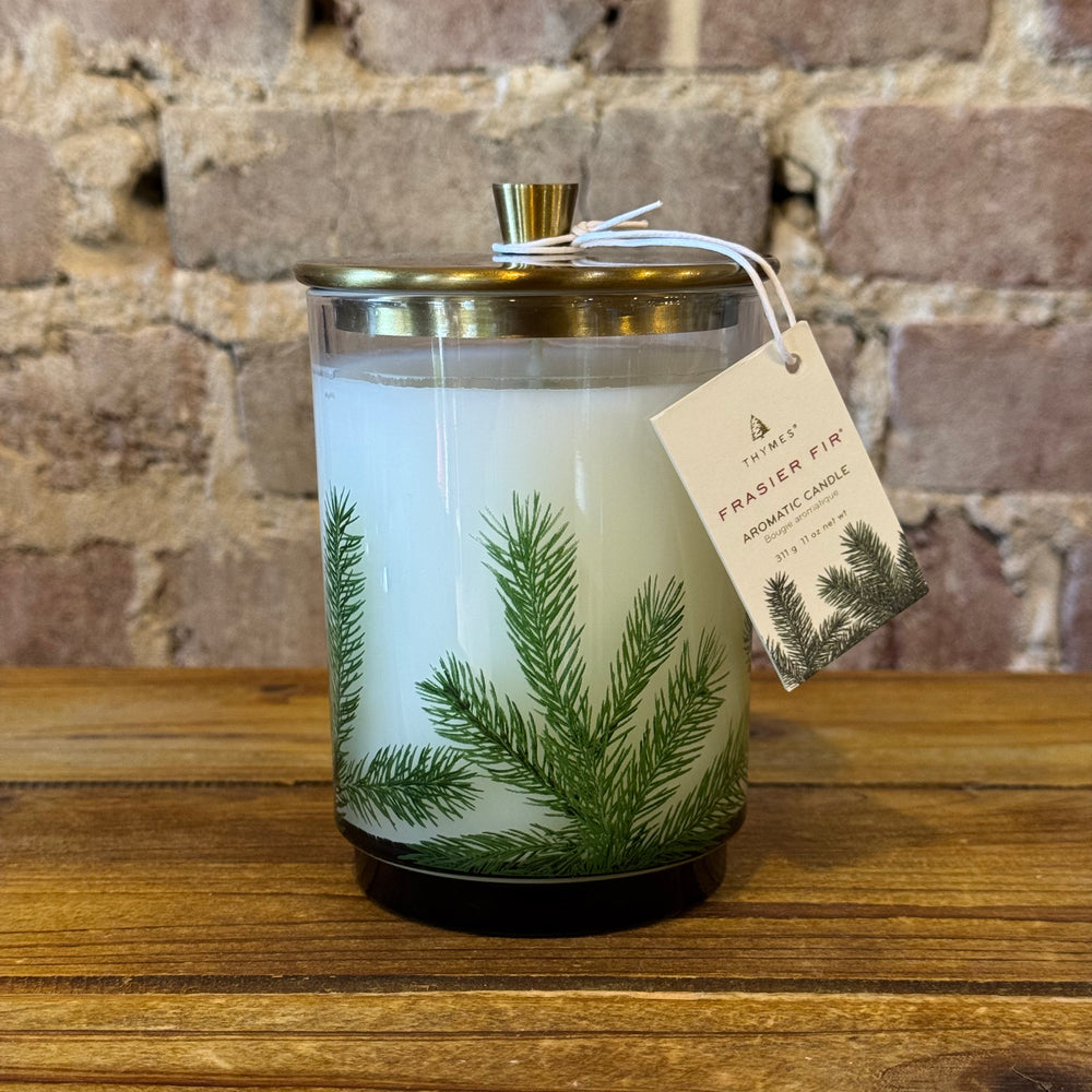 Candle with green leaf design and a tag on a wooden surface with a brick wall background