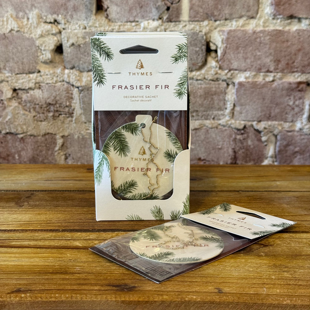 Thymes Frasier Fir decorative sachet packaging on a wooden surface with a brick wall background